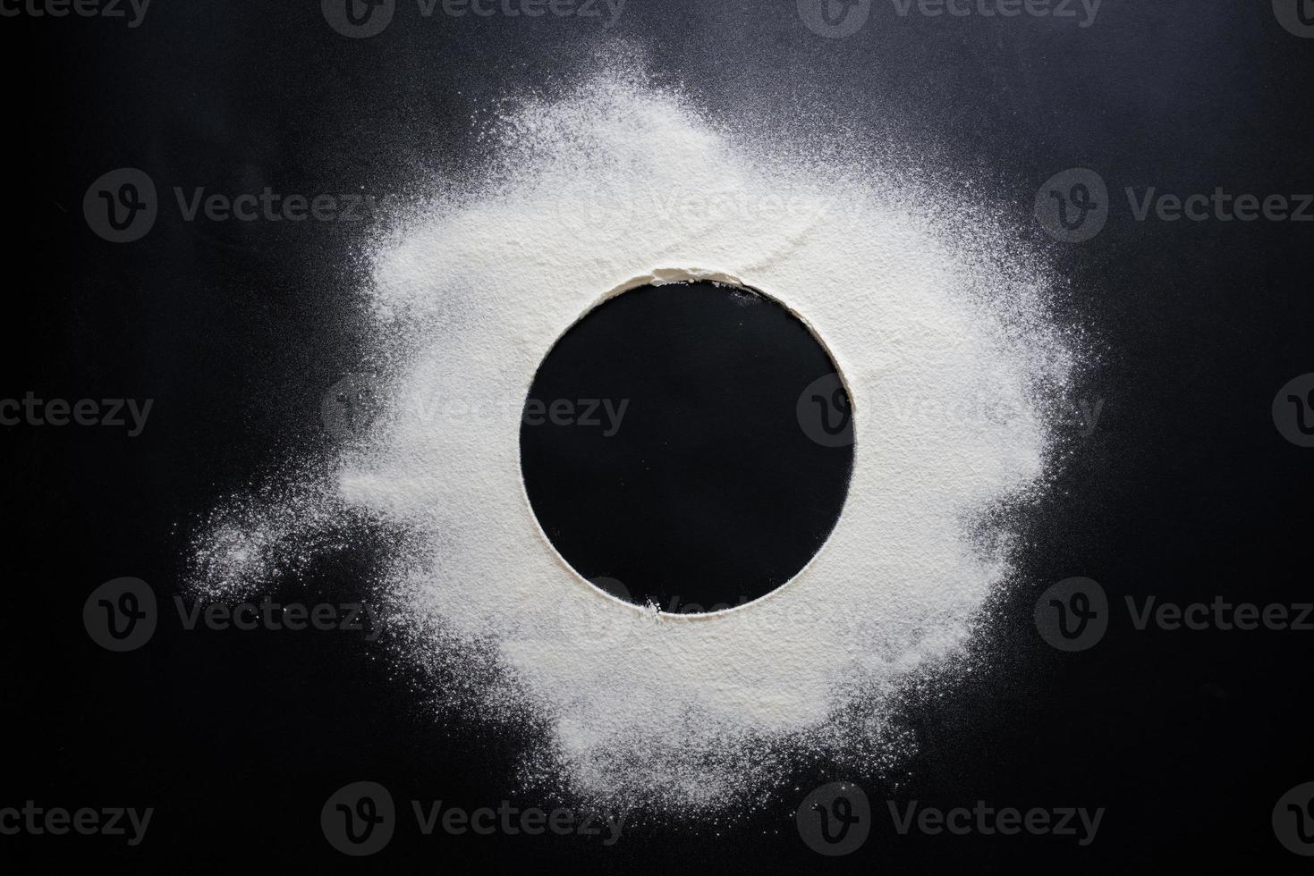 Abstract background. Sprinkled wheat flour circle, round spot on black. Top view on blackboard. Baking concept, cooking dough or pastry. photo