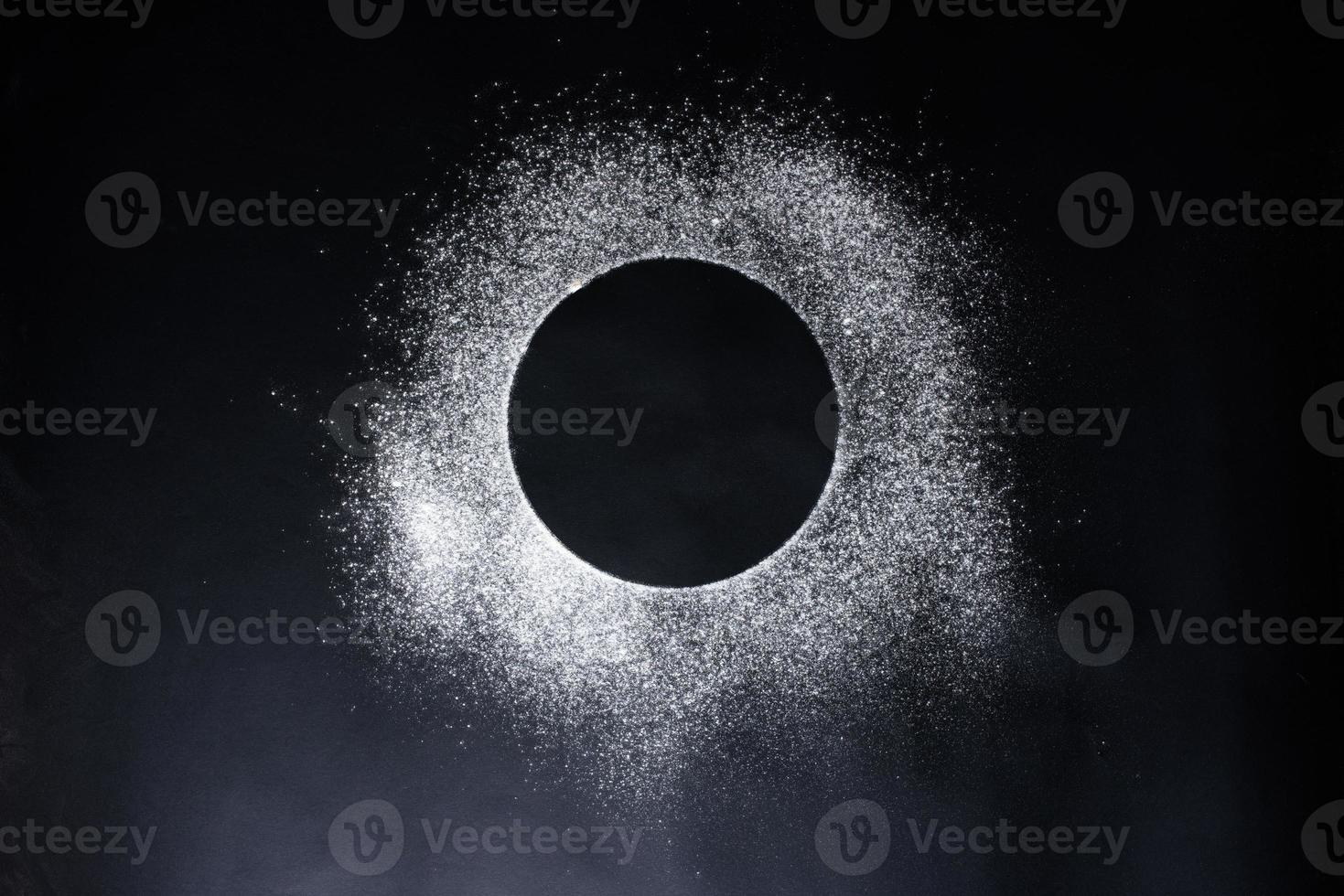 Abstract background. Sprinkled wheat flour circle, round spot on black. Top view on blackboard. Baking concept, cooking dough or pastry. photo