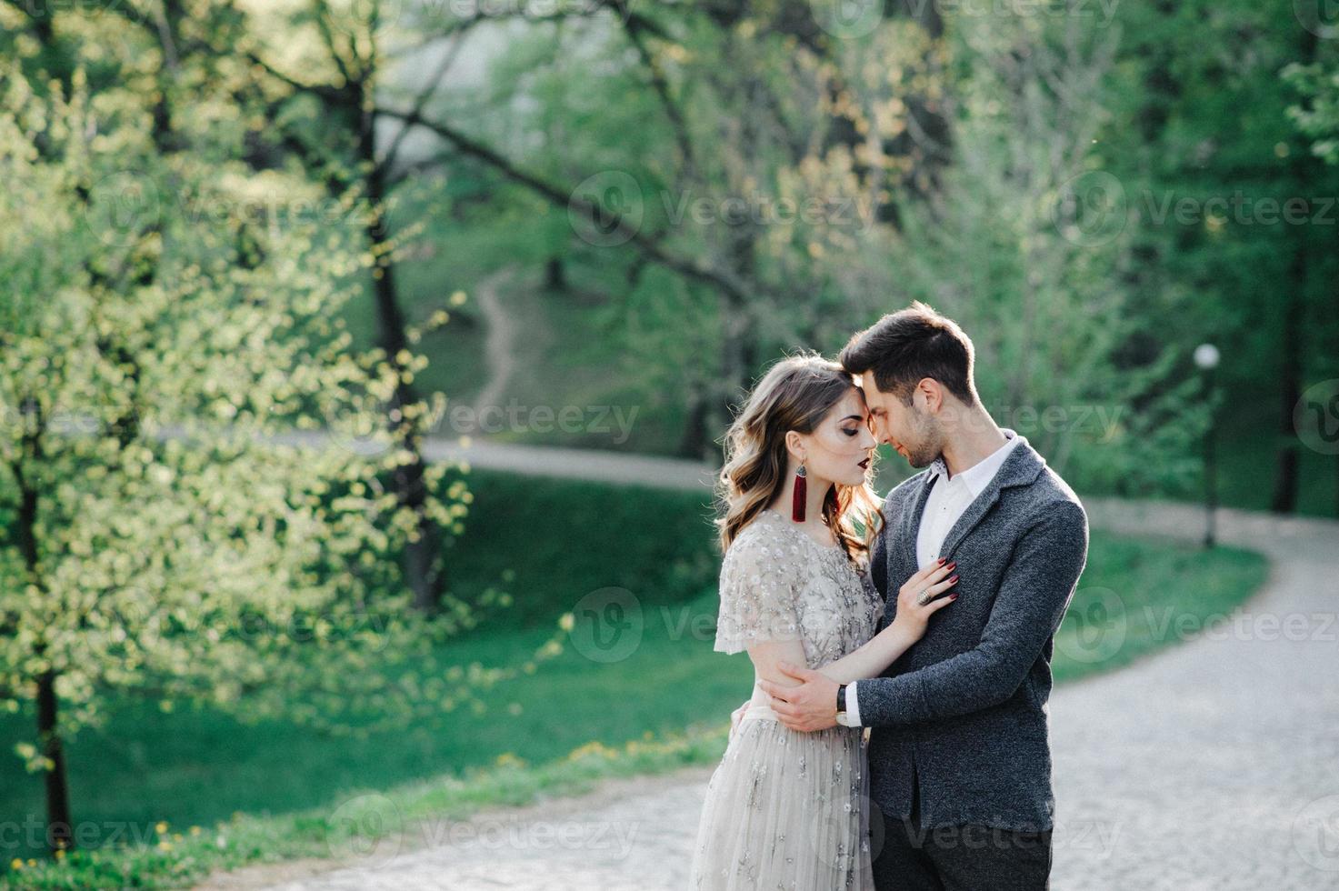 pareja vestida de boda con un ramo de flores y vegetación está en las manos contra el telón de fondo del campo al atardecer, la novia y el novio foto