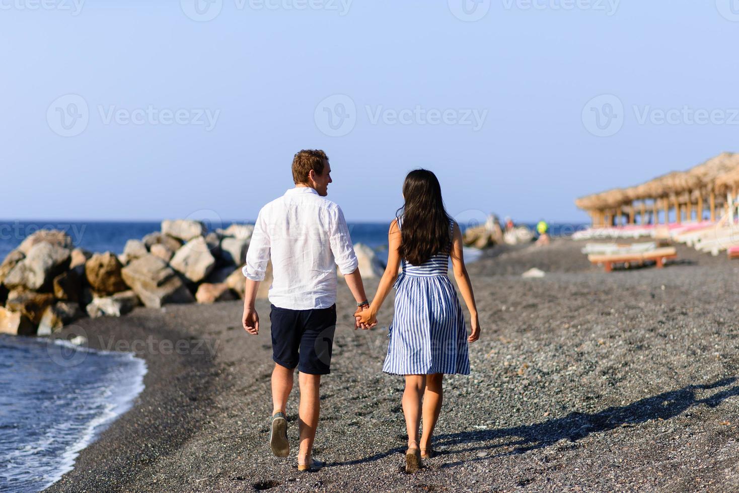 Young beautiful couple are walking on the background of the sea. Shot on Santorini Beach. photo