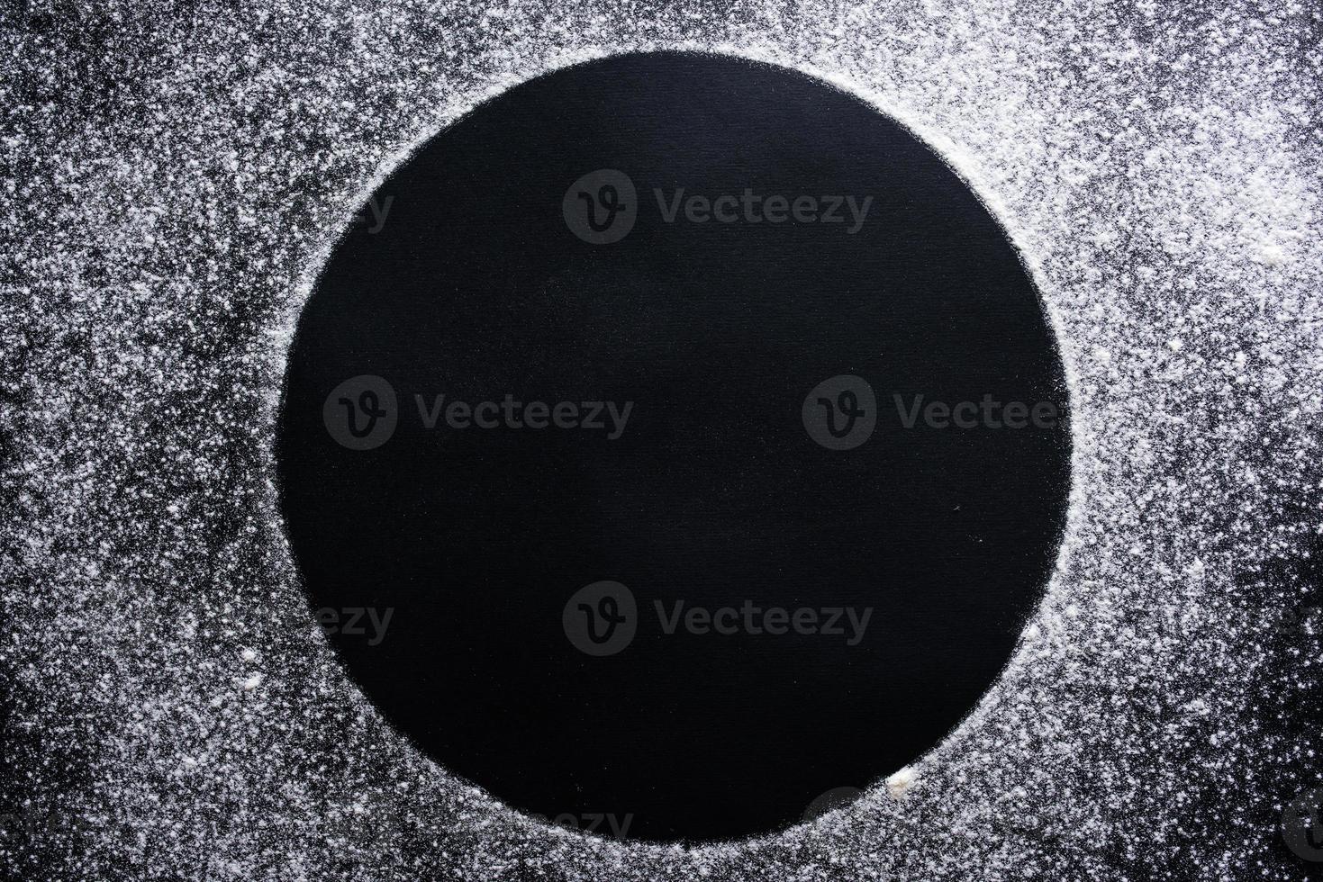 Abstract background. Sprinkled wheat flour circle, round spot on black. Top view on blackboard. Baking concept, cooking dough or pastry. photo