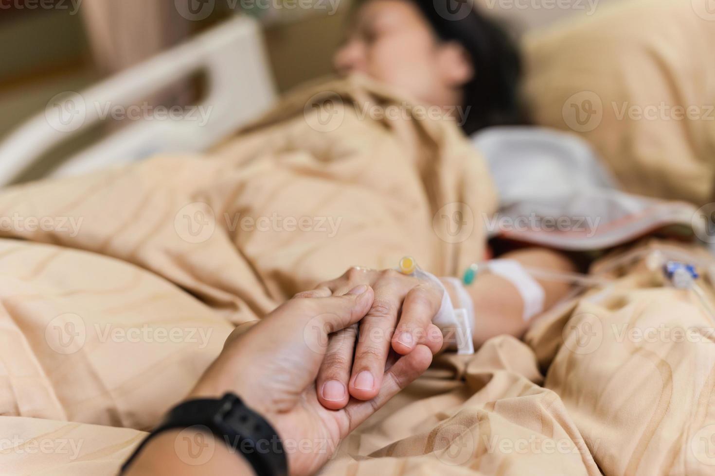 Husband hand holding his wife hand on bed in hospital room. photo