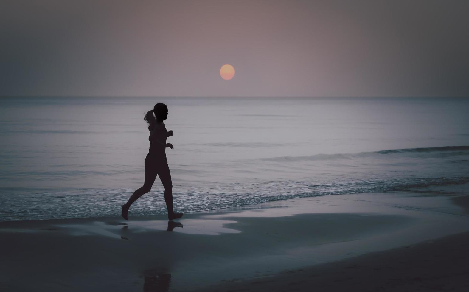 Silhouette of barefoot woman running on the beach at sunrise. photo