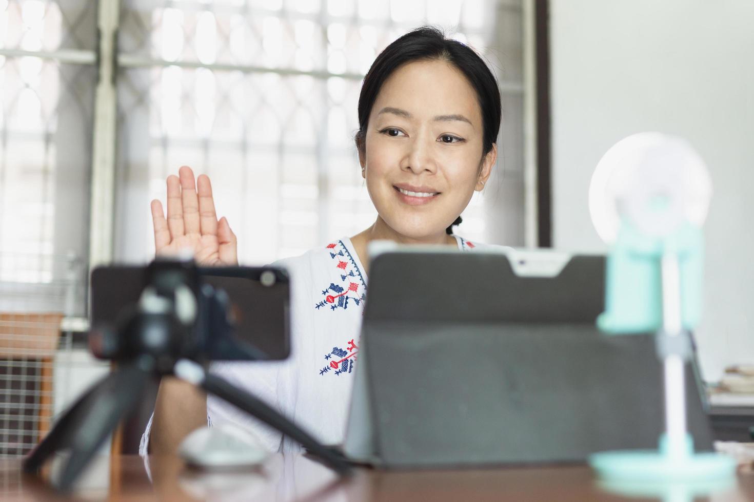 Woman waving hand greeting viewer using smartphone online broadcasting live. photo