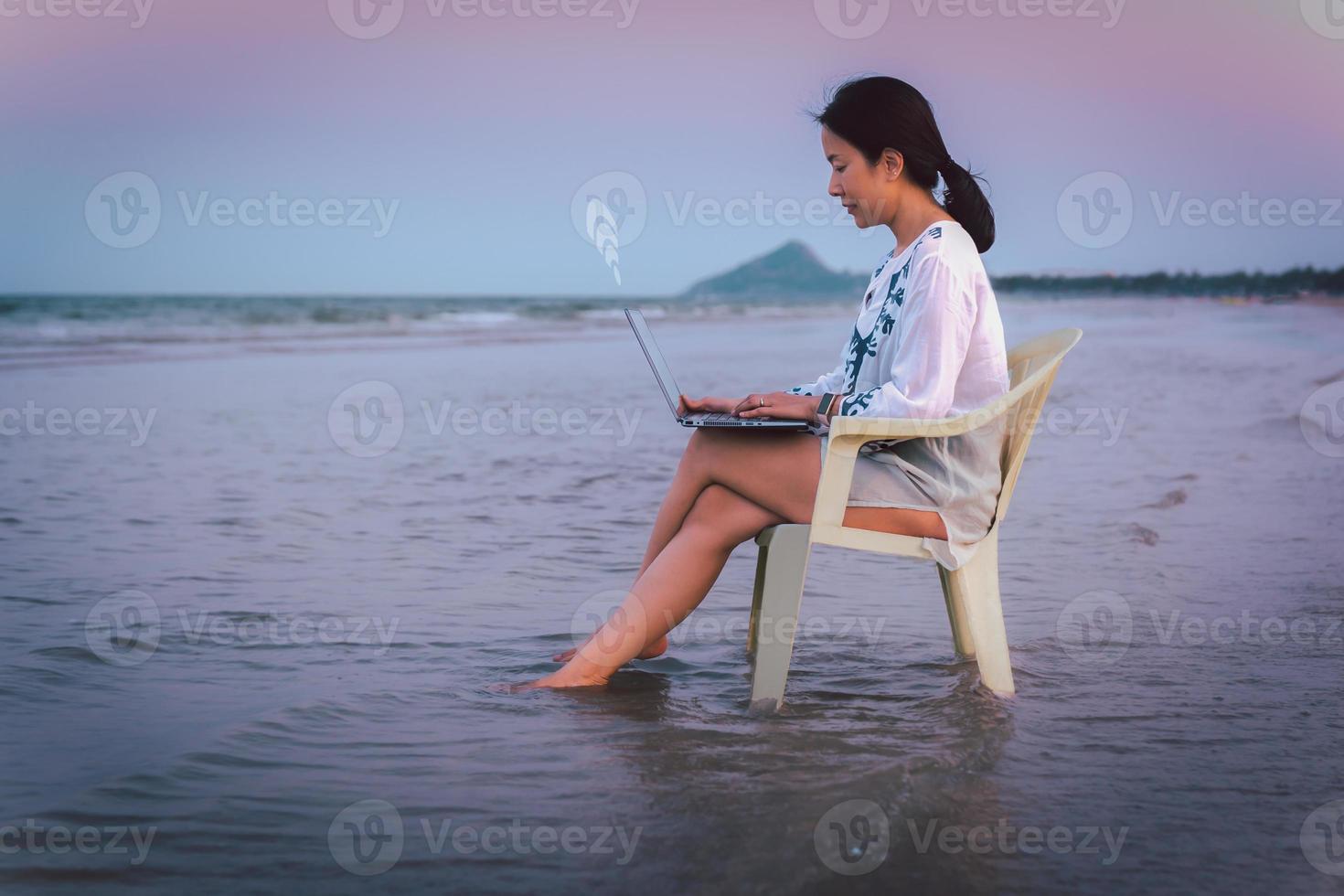 Side view businesswoman using laptop while sitting in a chaie on the beach. photo