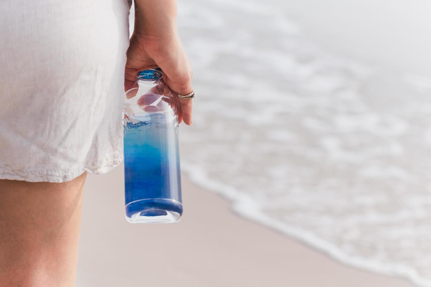 Woman in short standing on the beach holding bottle of water. photo