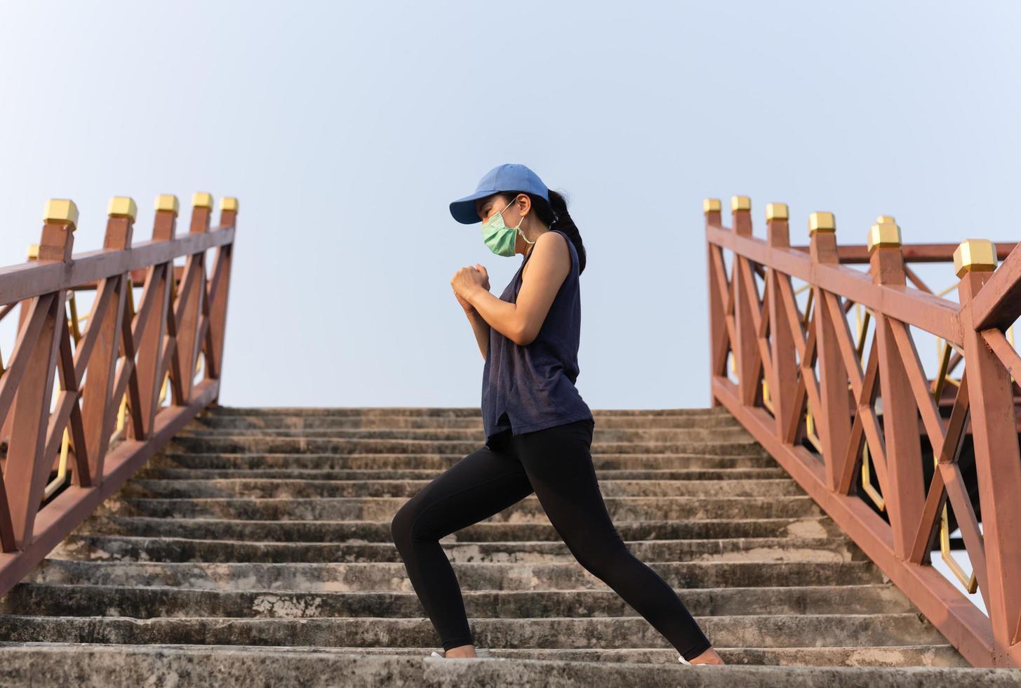 Fit woman in medical mask doing stretching on the stairs in the open air. photo