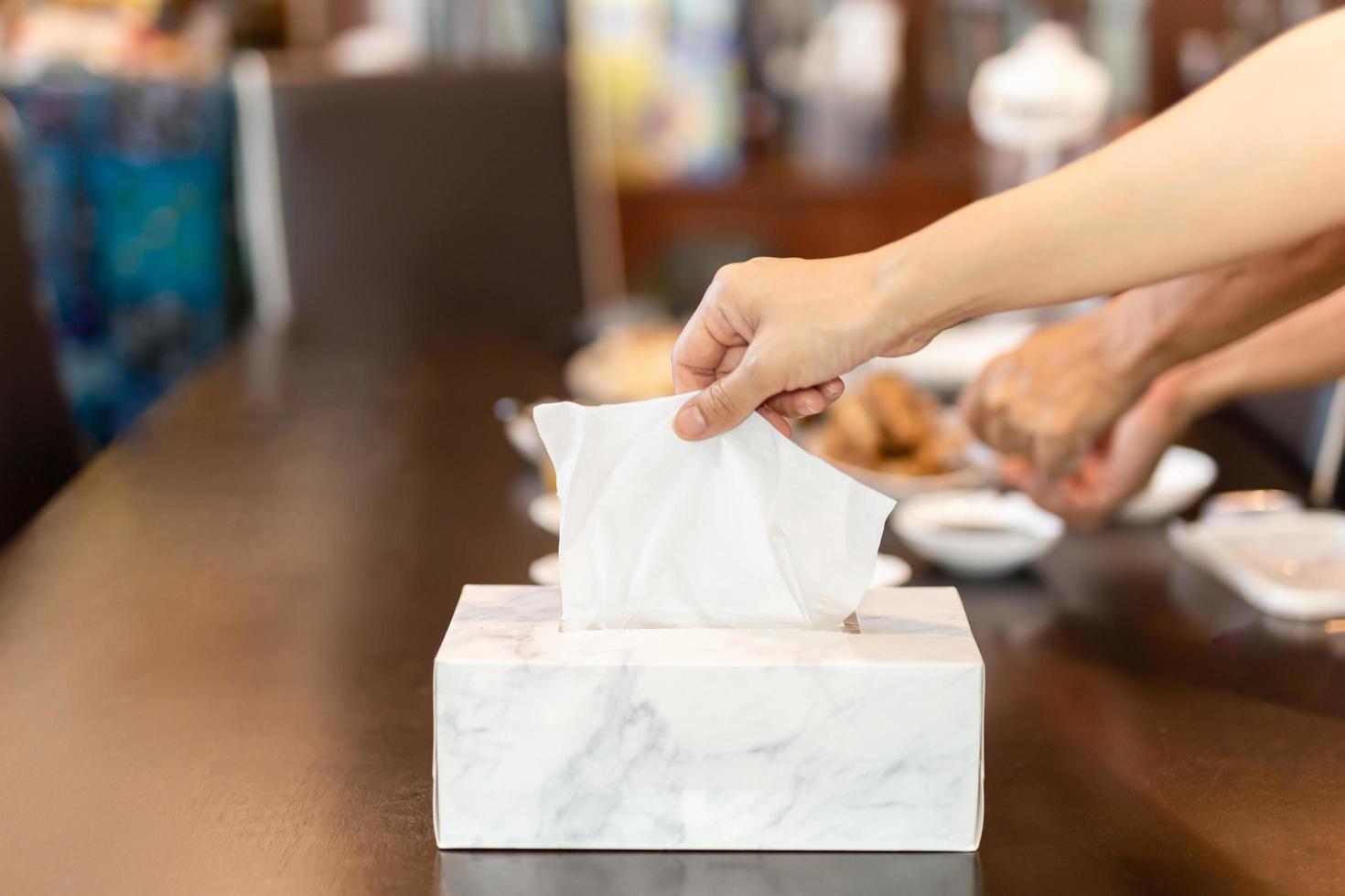 Woman hand picking up tissue paper from tissue box on dinner table. photo