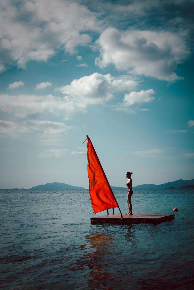 mujer de belleza y moda en traje de baño de pie en una balsa de madera en el océano. foto