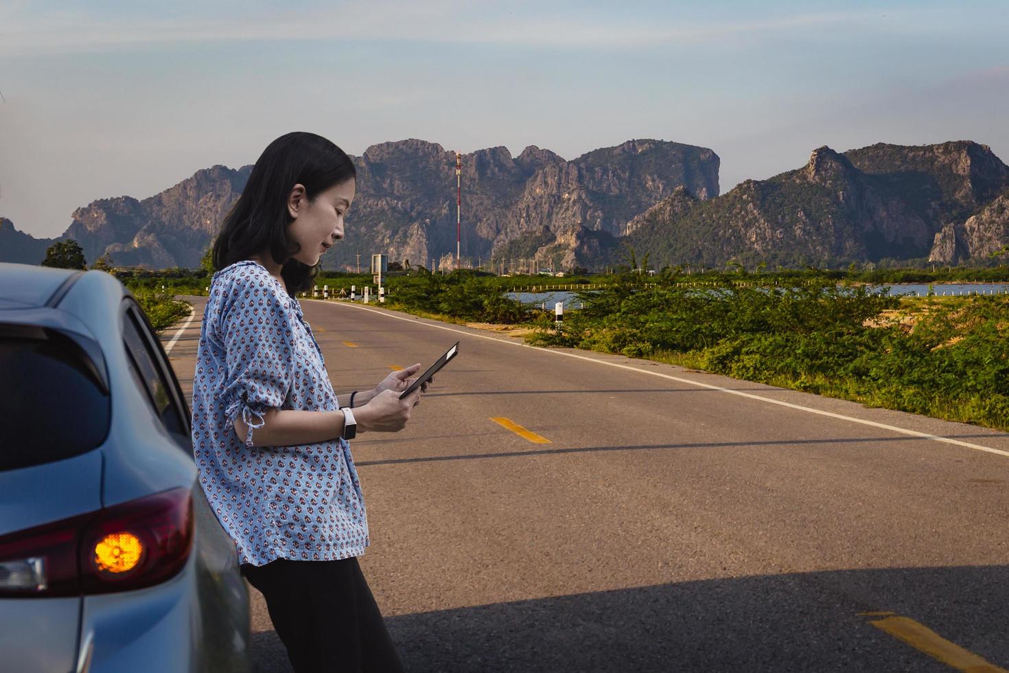 Woman standing next to car trying to get signal on mobile phone. photo