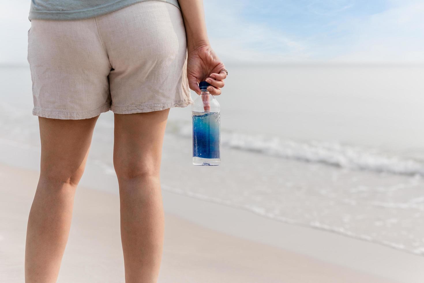 Woman in short standing on the beach holding bottle of water. photo