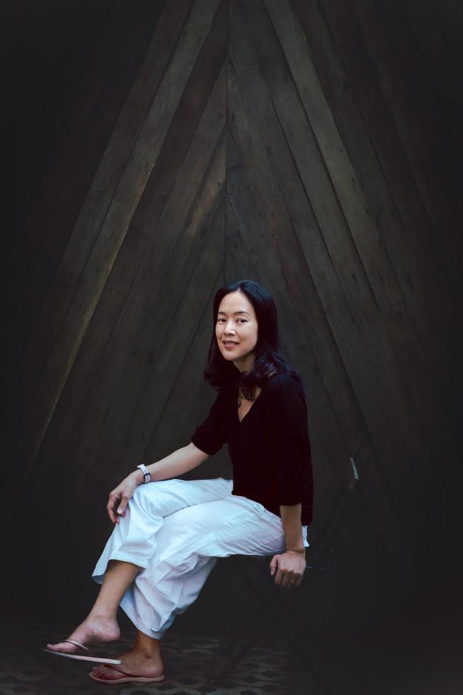 Full body portrait of asian woman sitting on chair on wooden background. photo