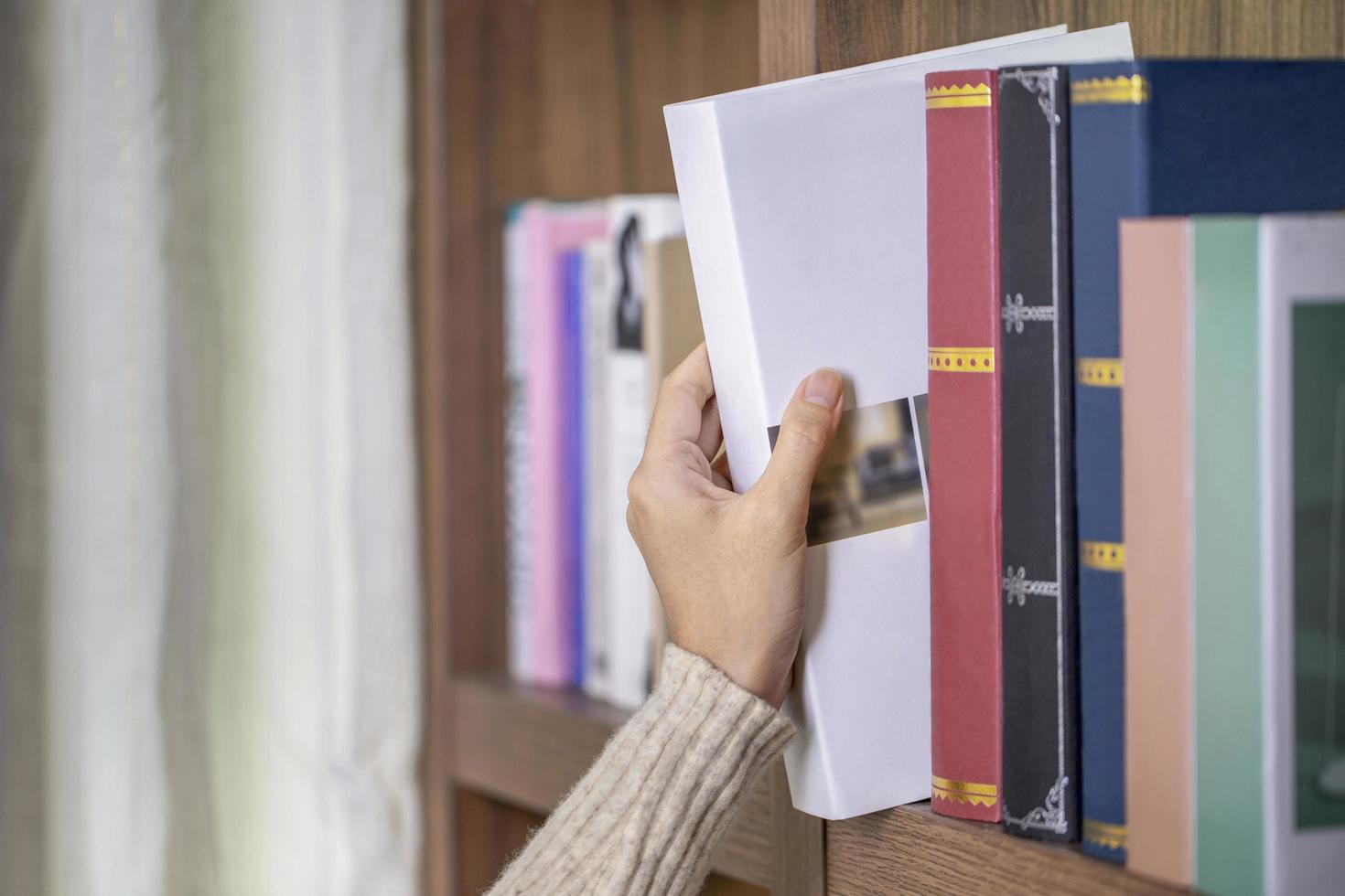 Close up shot hand of young woman taking book from library bookshelf photo