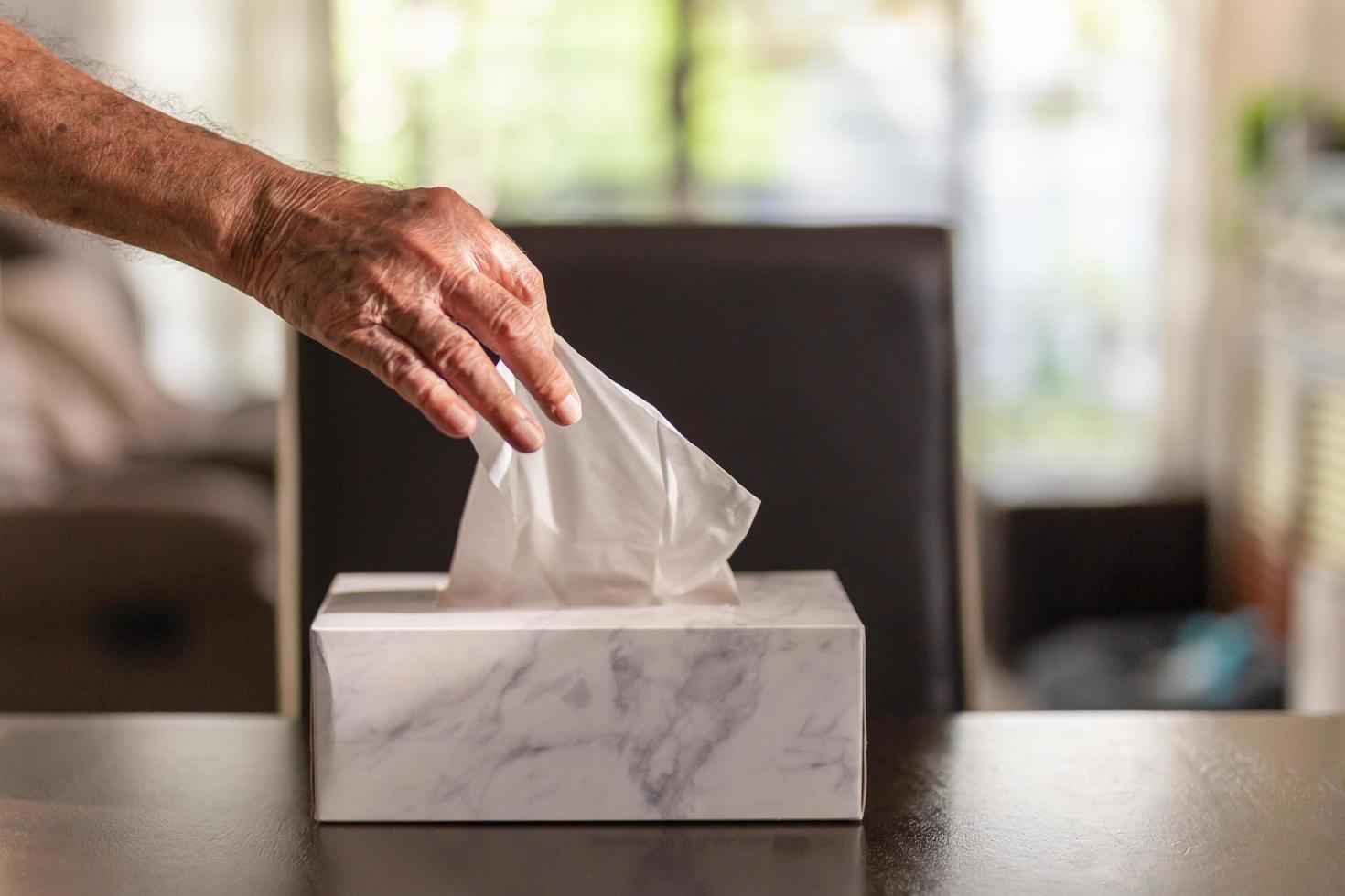 hombre mayor mano recogiendo papel de seda de la caja de pañuelos en la mesa de la cena. foto