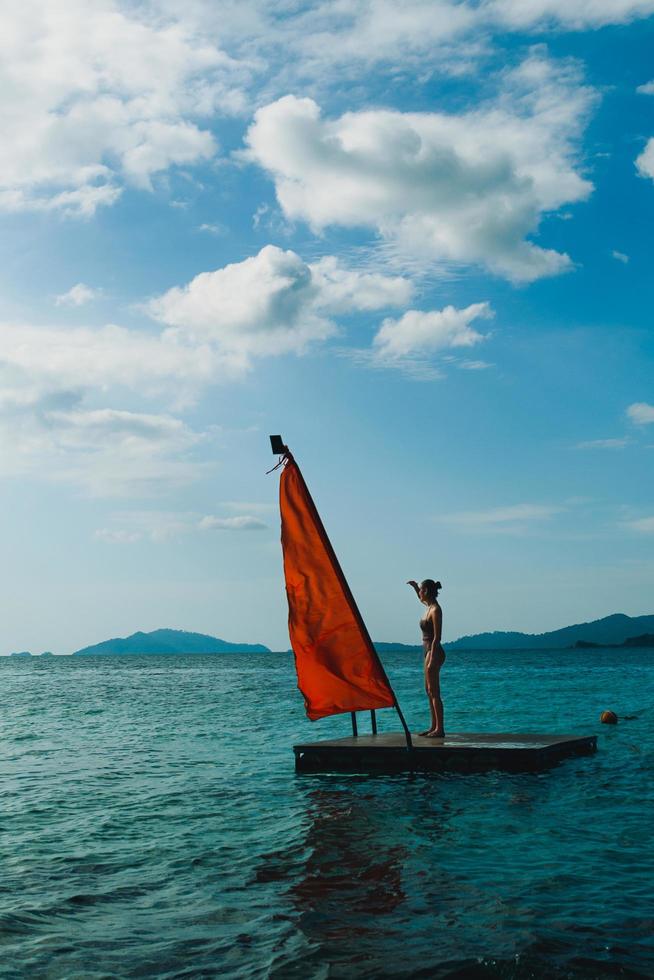 Beauty and fashion woman in swimming suit standing on wooden raft in the ocean. photo