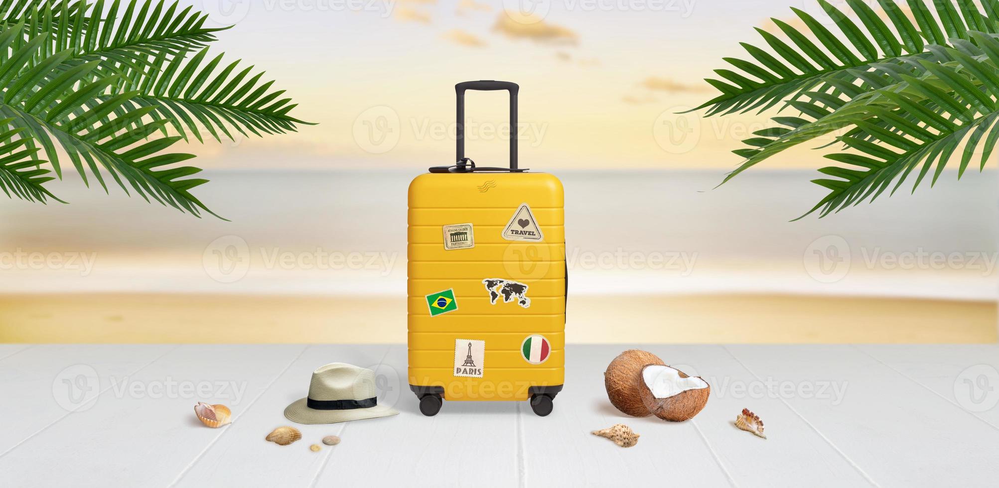 Suitcase with travel stickers on beach surrounded by hat, coconuts, shells and palm leaves. Travel concept photo