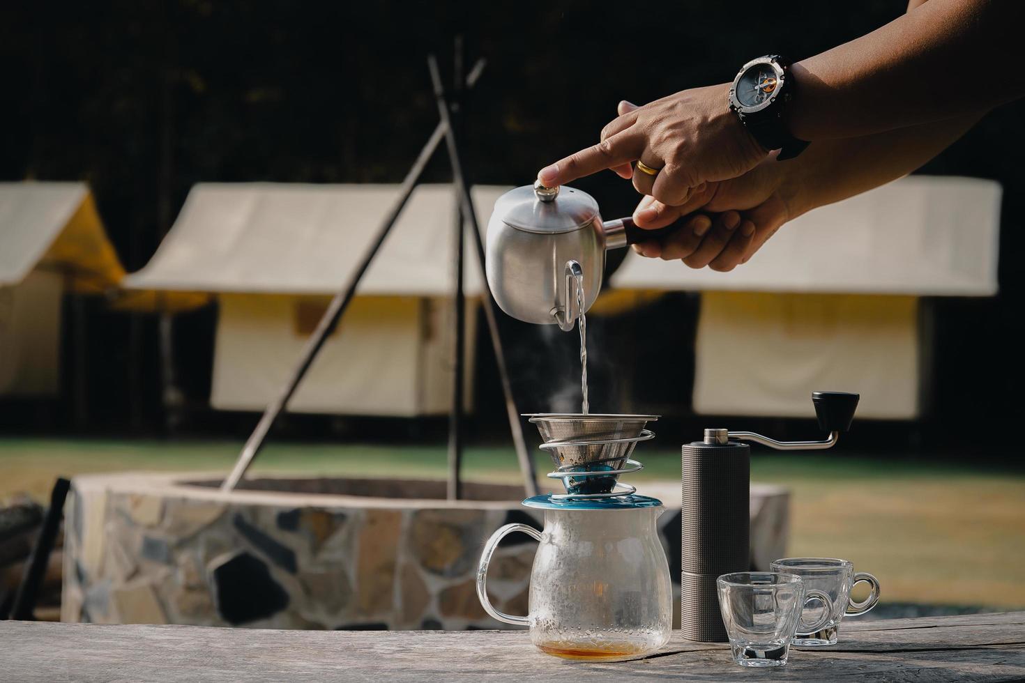 hombre de café por goteo vertiendo agua en café molido con filtro en el campamento. foto