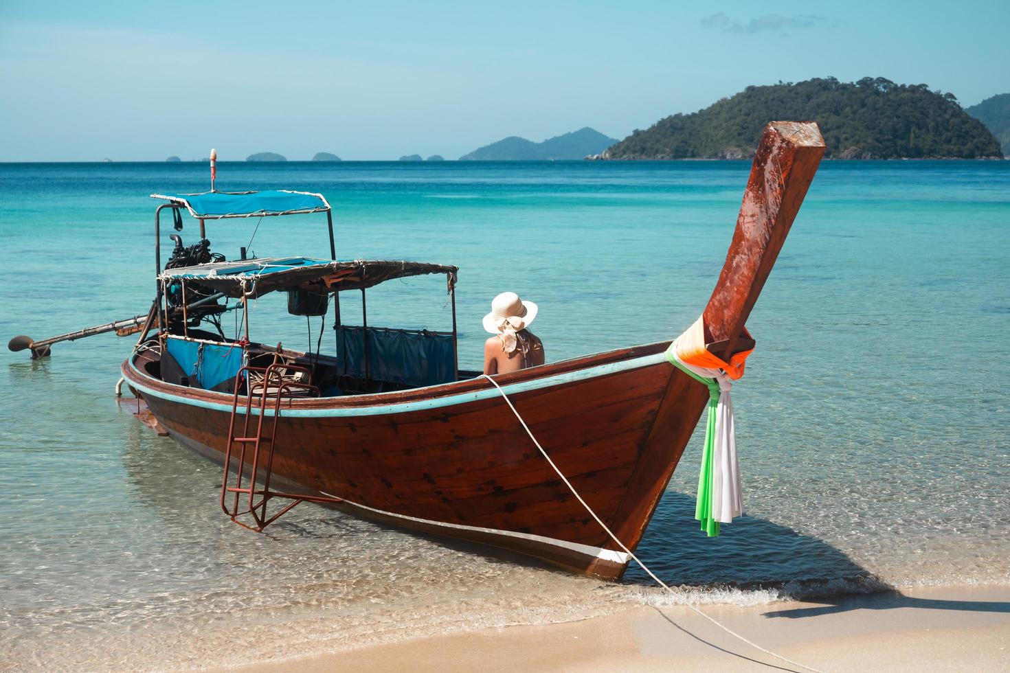 Unidentified woman sitting on a wooden boat in the sea sun bathing. photo