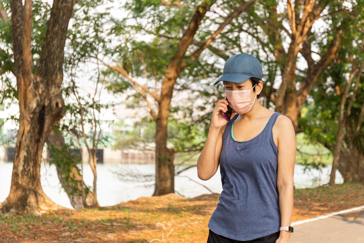 mujer usa ejercicio de máscara médica caminando en el parque hablando por teléfono celular. foto