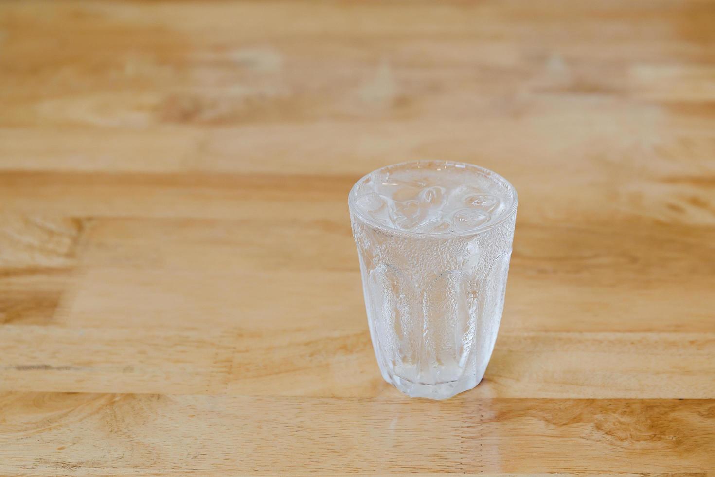 Glass of fresh water with ice cube on wooden table. photo