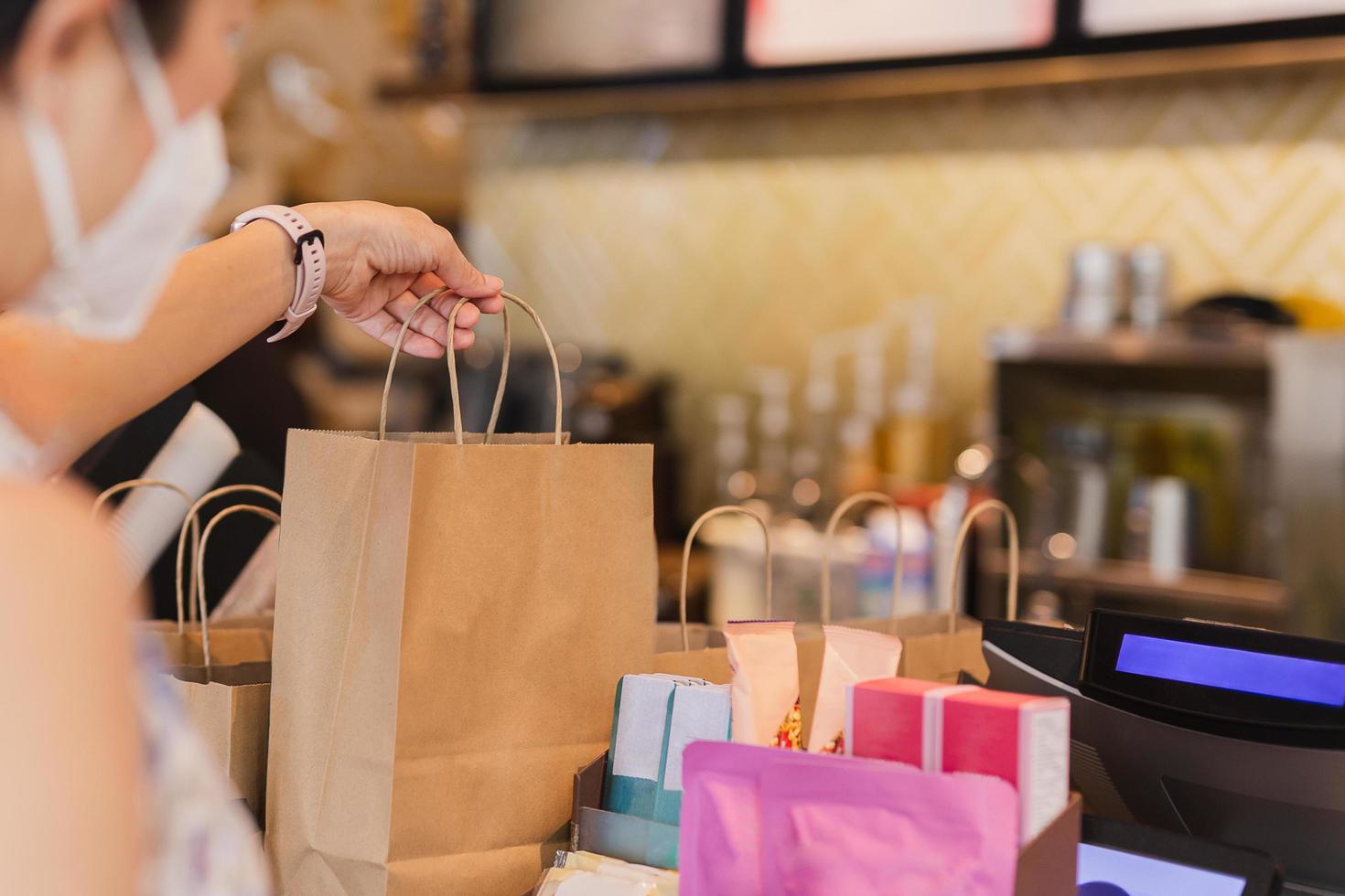 Waitress at counter giving eco friendly paper bag with take away drink in cafe. photo