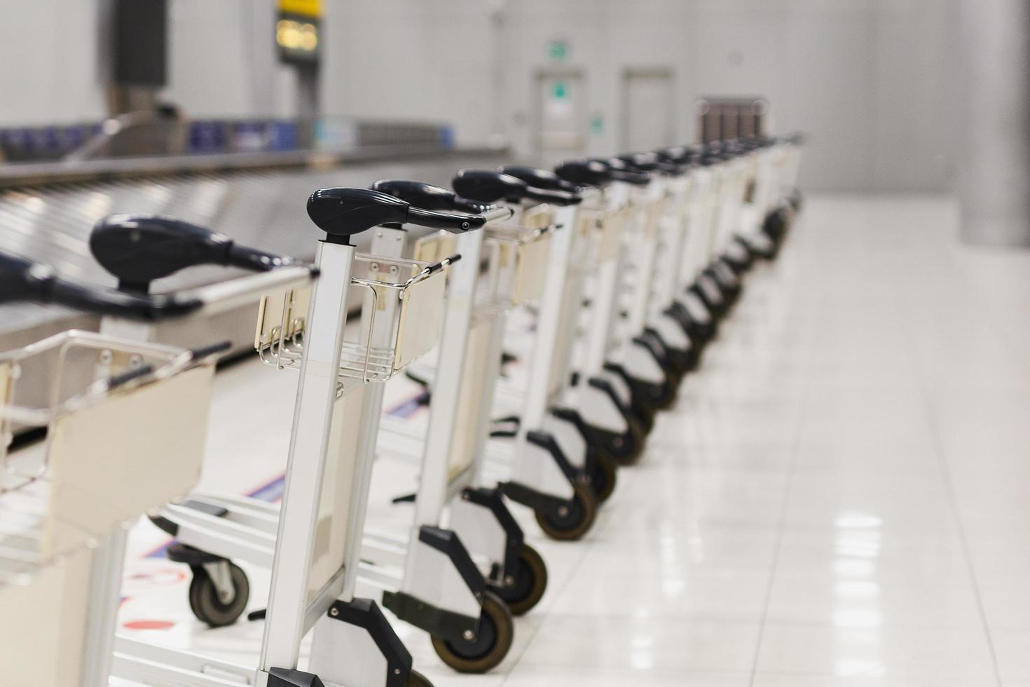 carros de equipaje vacíos del aeropuerto estacionados detrás de la línea de advertencia en el área de reclamo de equipaje en la terminal. foto