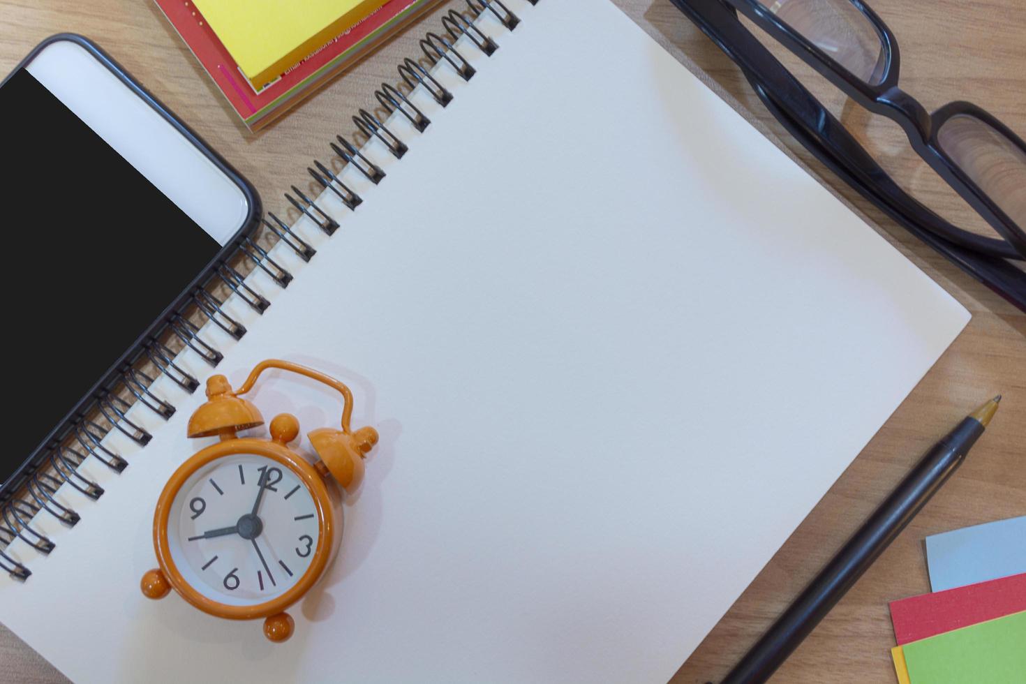 Notepad with alarm clock on wooden desk. Flat lay. Directly above photo