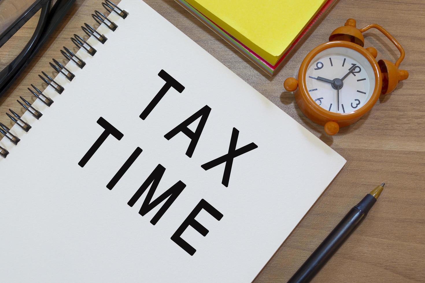 Tax time text on notepad with alarm clock on wooden desk. Business concept photo