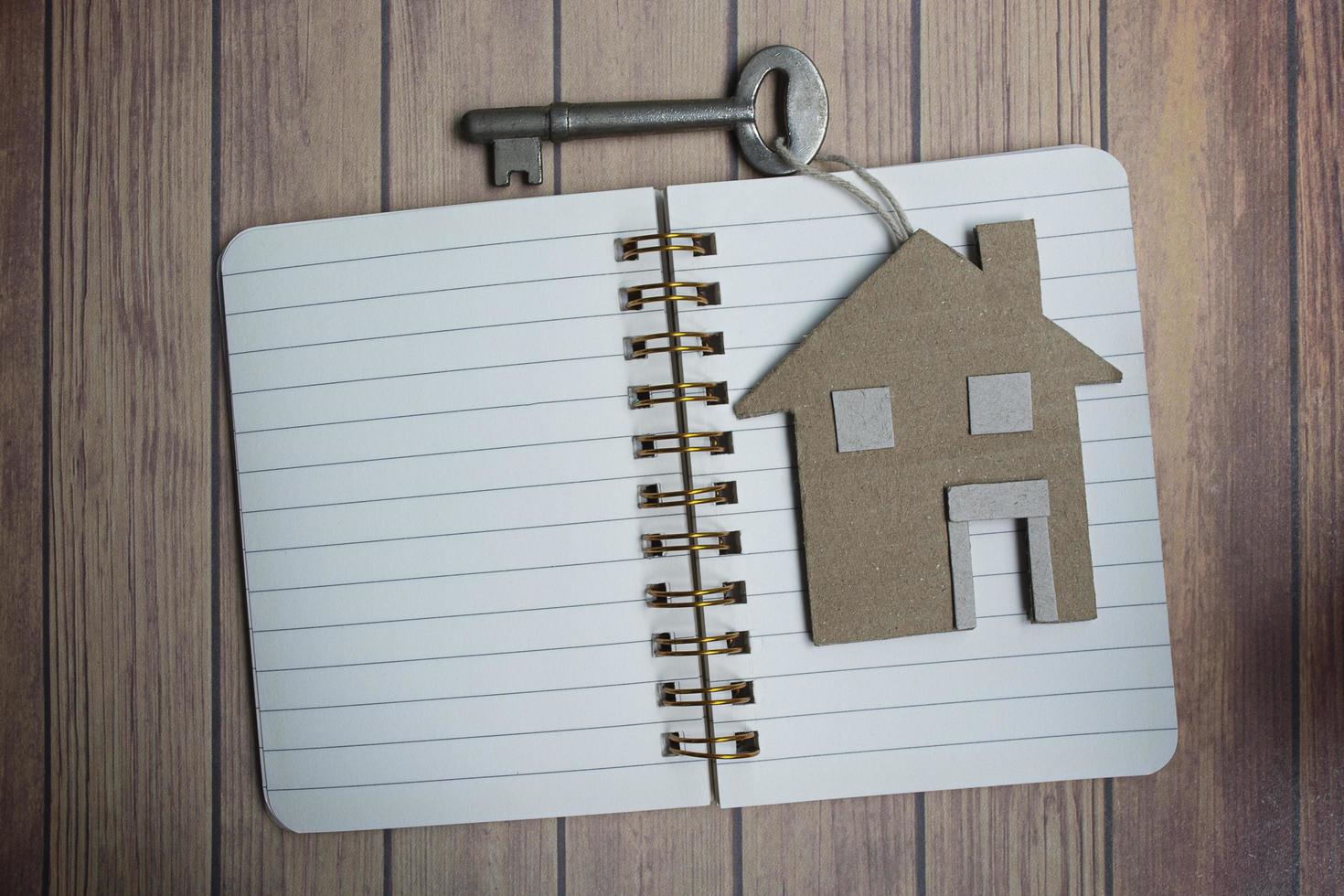 Notepad with house model and key on wooden desk. Directly above. Flat lay. photo