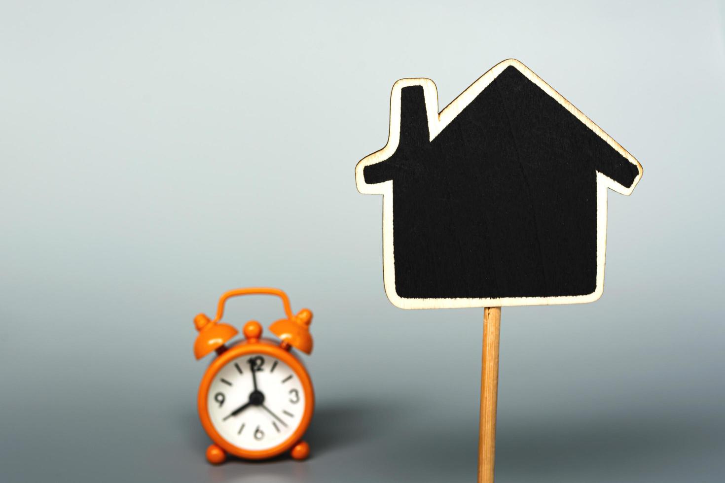 Wooden house with background of alarm clock. Real estate concept. Copy space. photo