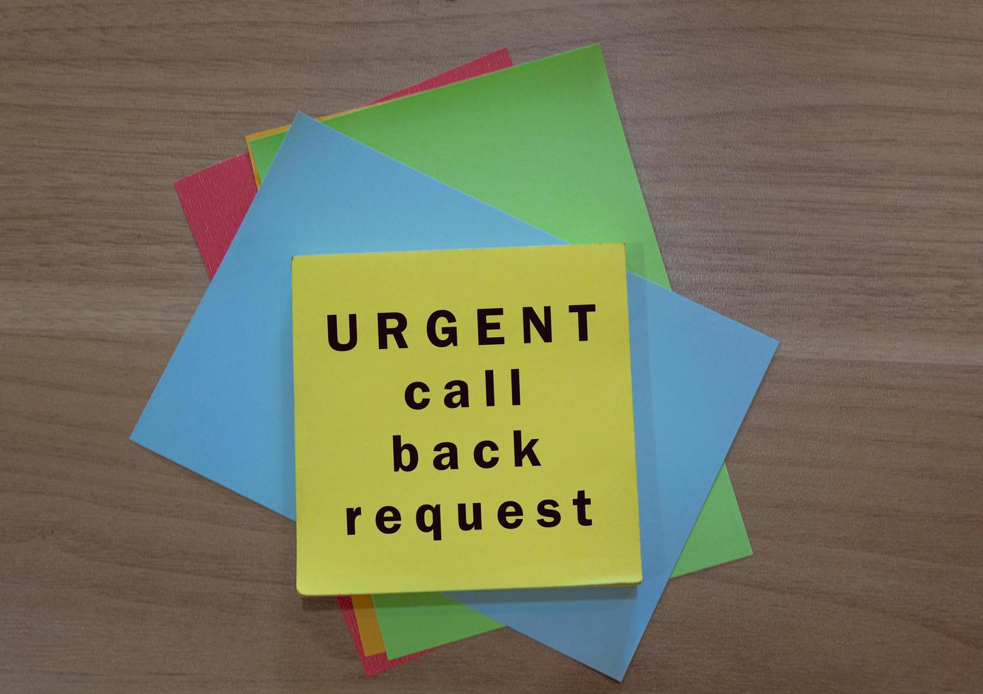 Urgent call back request text on colorful notepad on wooden background photo