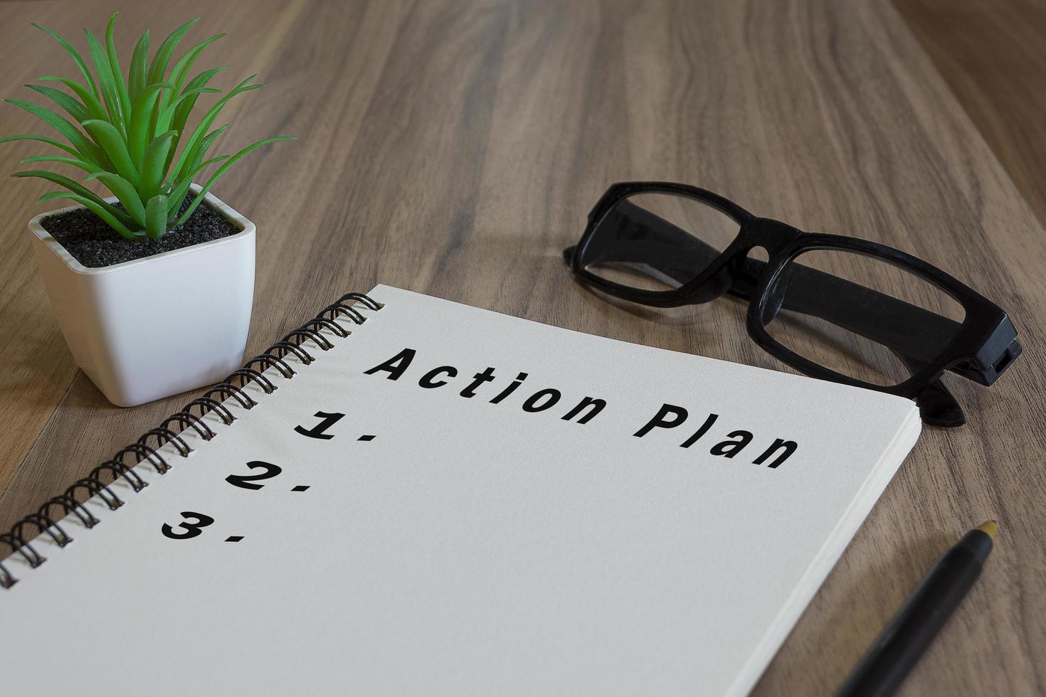texto del plan de acción en el bloc de notas blanco con plan en maceta, gafas y un bolígrafo en el escritorio de madera foto