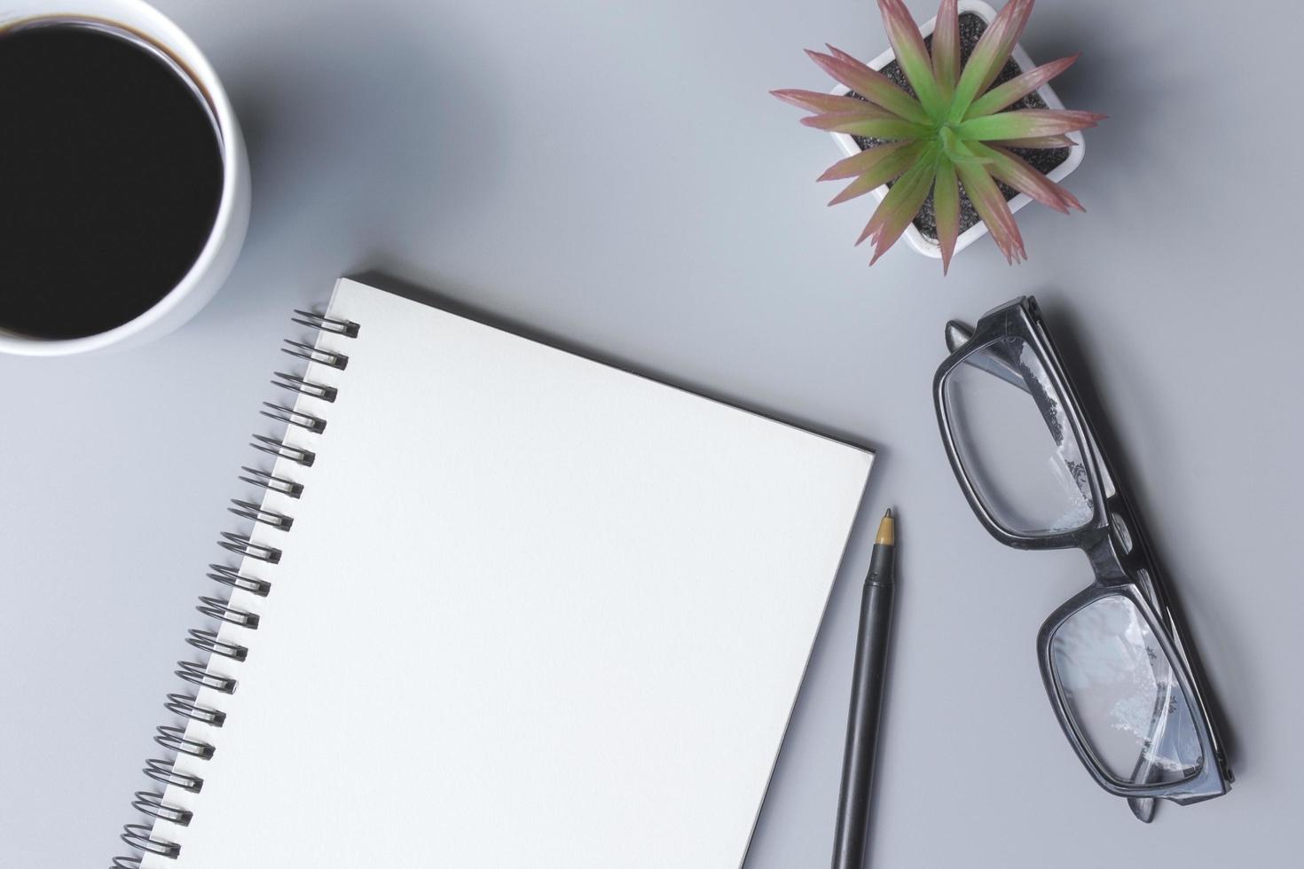 Notepad with coffee cup, glasses, pen and potted plant on a desk. Flat lay photo