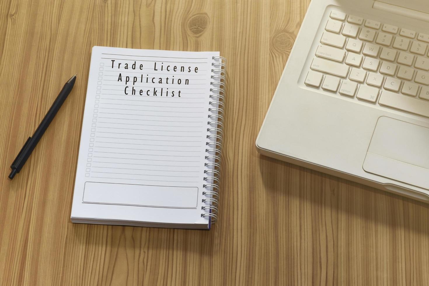 Text on notepad with laptop and pen on wooden desk - Trade license application checklist photo