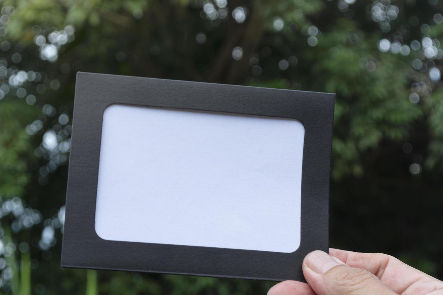 manos sosteniendo papel enmarcado en blanco con fondo borroso de árboles foto
