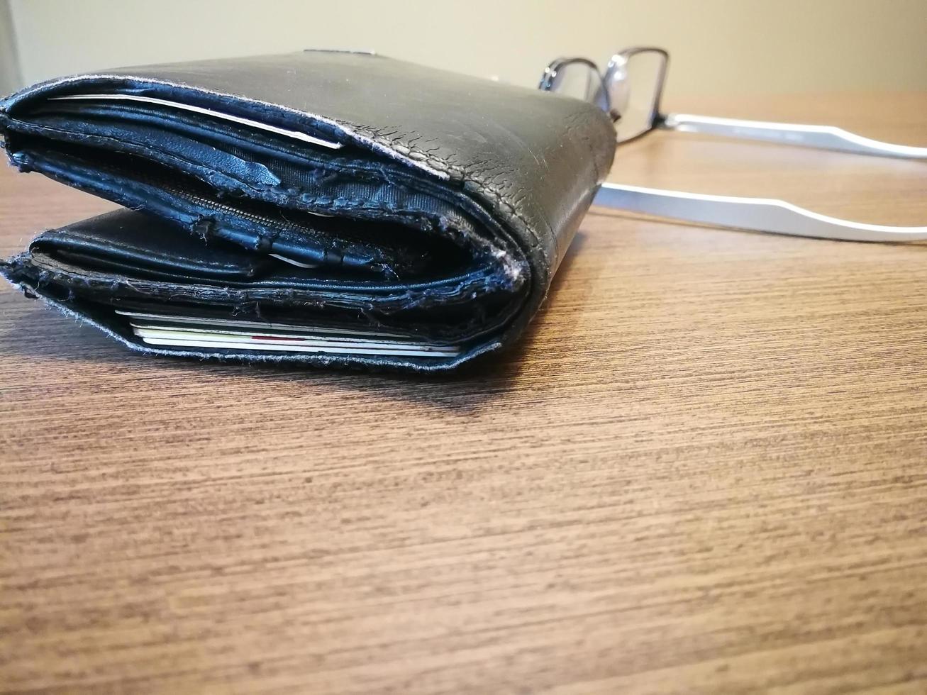 Closeup old wallet on the wooden desk with reading glasses. Debt concept photo