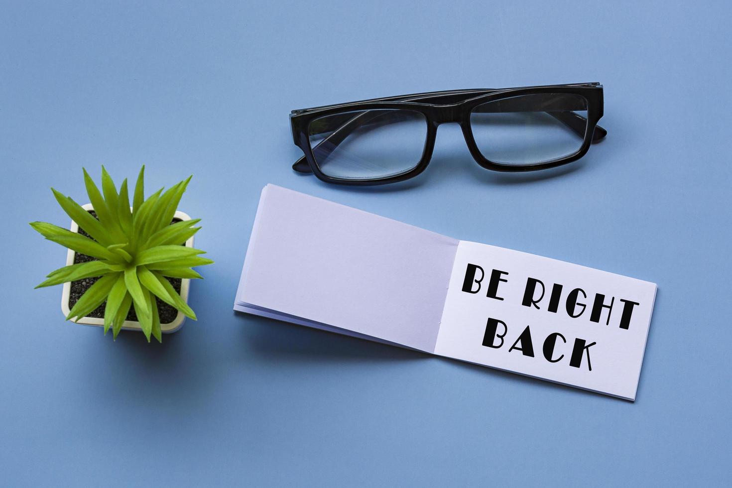 Be right back text on notepad with reading glasses and potted plant. photo