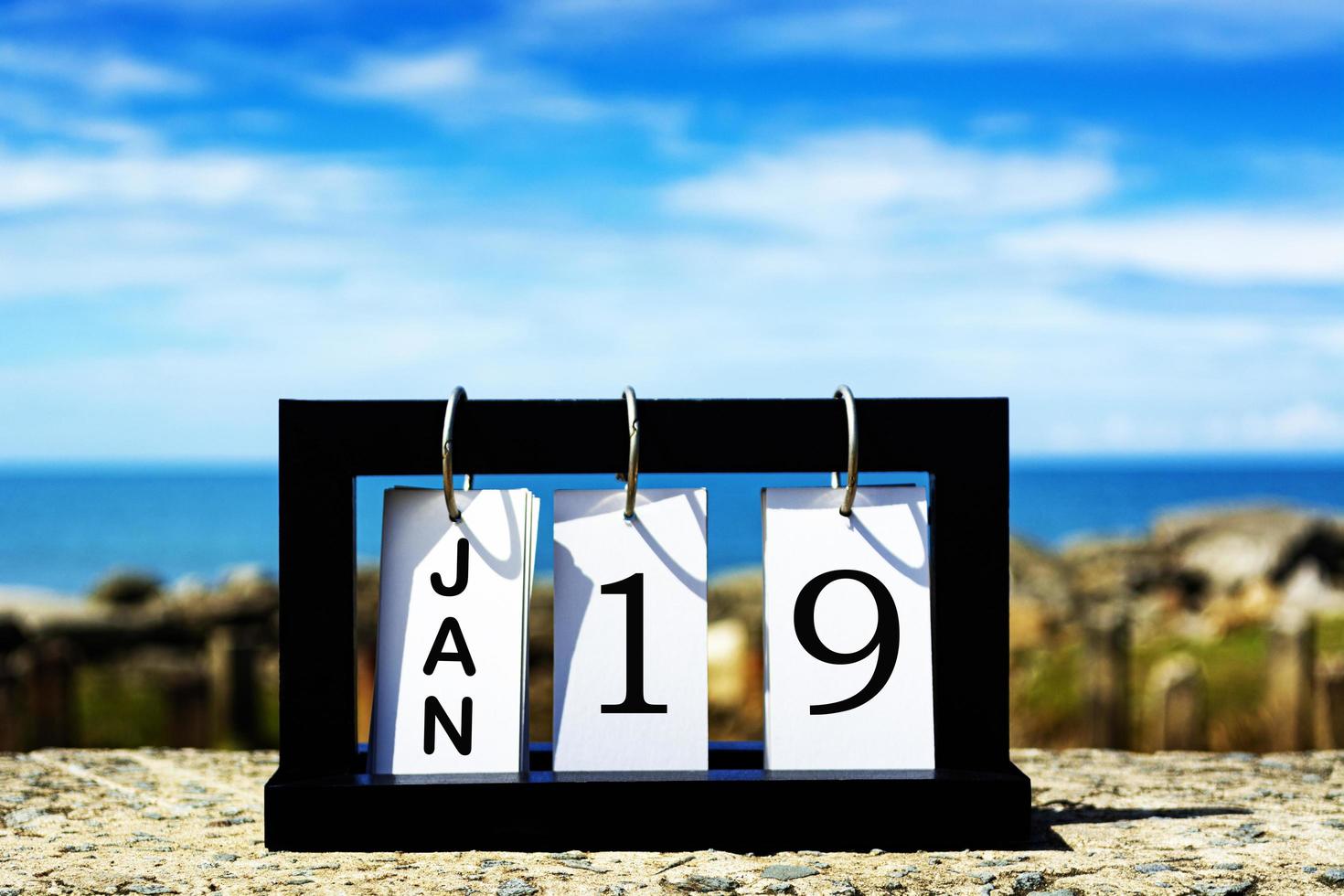19 de enero texto de fecha de calendario en marco de madera con fondo borroso del océano foto