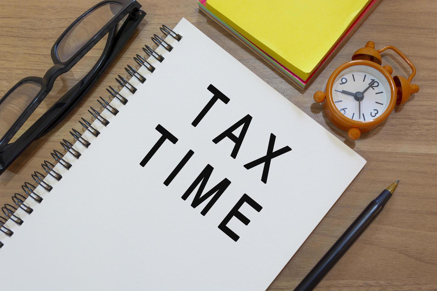 Tax time text on notepad with alarm clock on wooden desk. Business concept photo