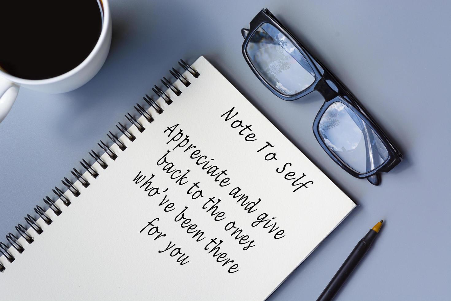 Motivational quote on notepad with coffee and reading glasses on a desk. photo