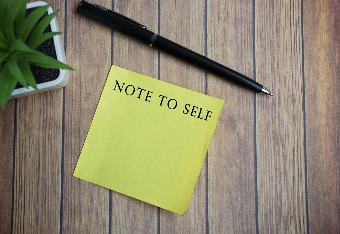 Note to self text on yellow stick note on wooden table photo