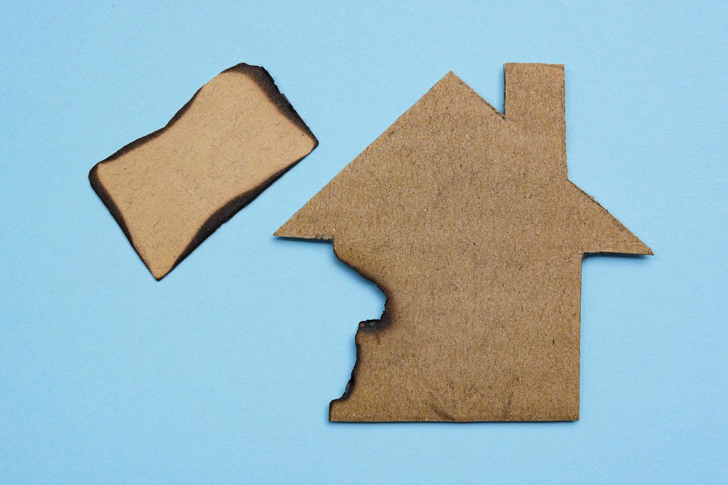 Burned paper house model on blue background. Home insurance concept. photo