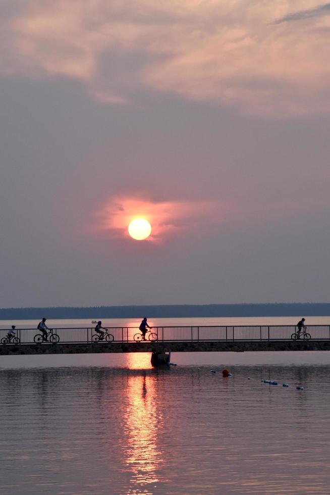 the setting sun creates silhouettes of cyclists riding over a bridge photo