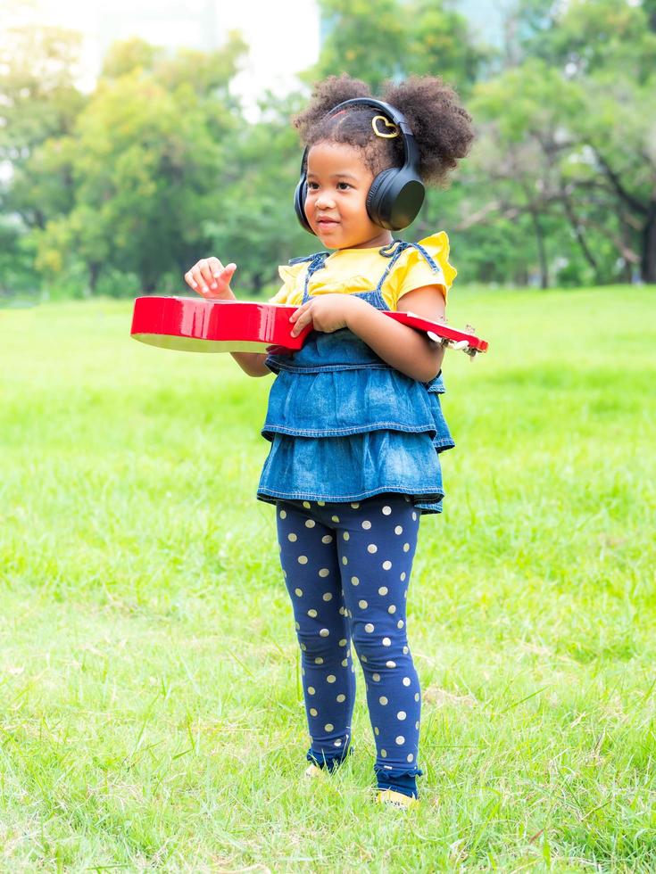 la niña se para en el césped, usa audífonos y está aprendiendo a tocar cuerdas de ukelele foto