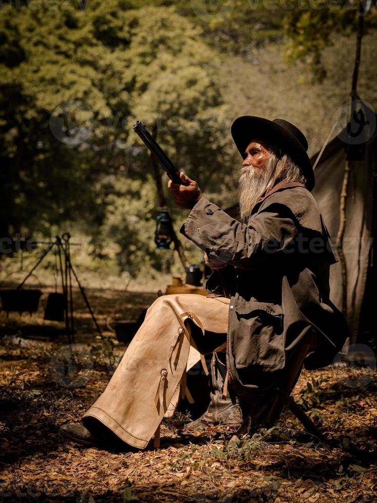 A senior cowboy sat with a gun to guard the safety of the camp in the western area photo