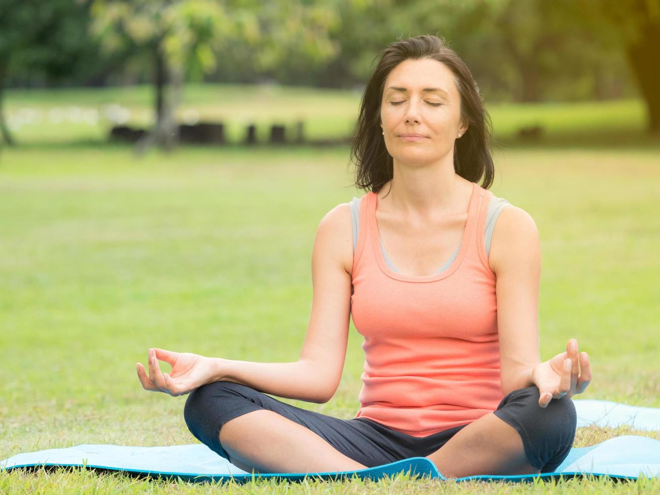 European women sitting, arms stretching, meditation and relaxing during the morning hours by yoga in an outdoor park photo