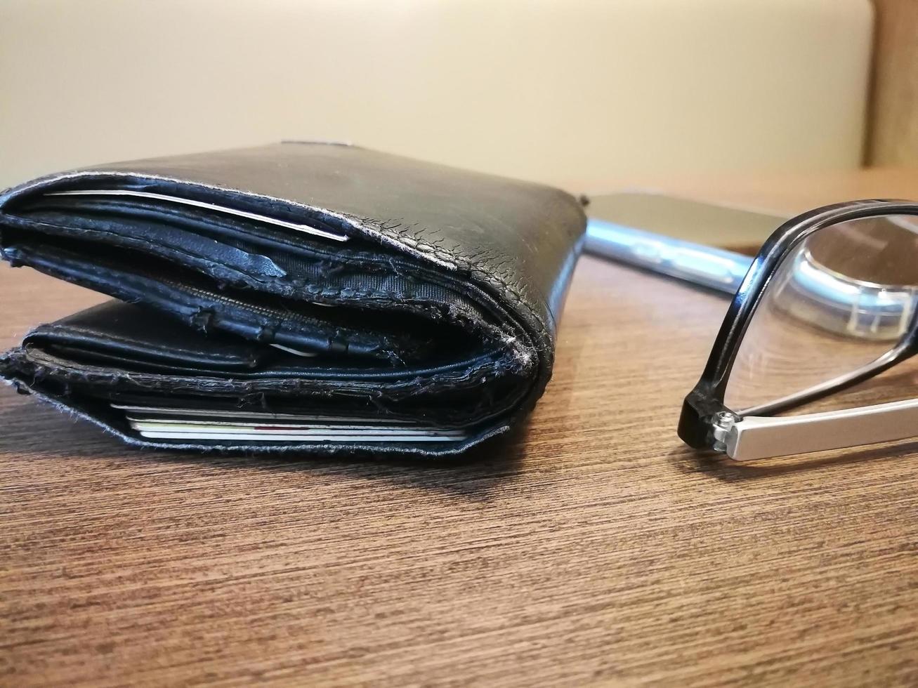 Blurred background of old wallet on the wooden desk with reading glasses and smartphone photo