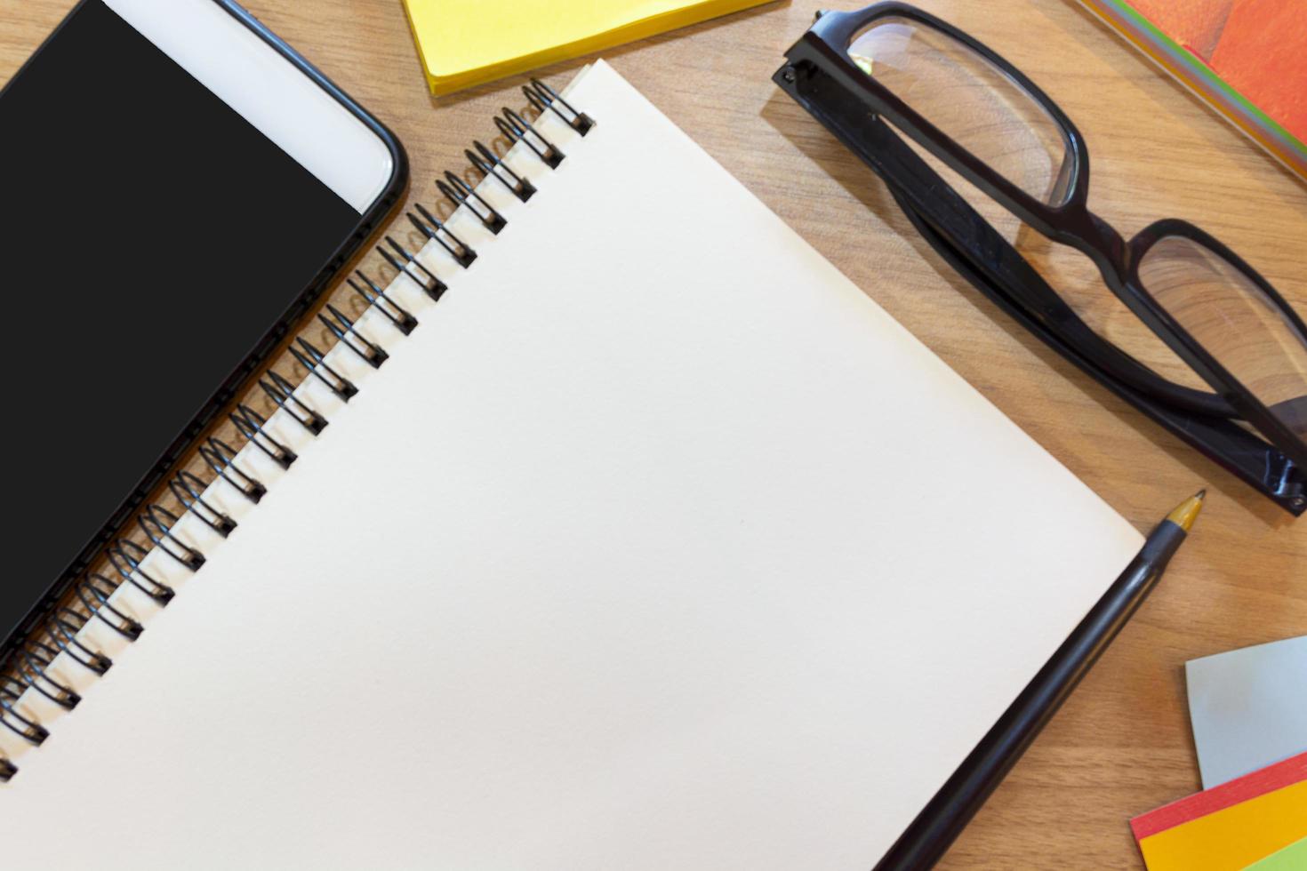 Notepad with yellow note, pen, study glasses and smartphone on wooden desk photo