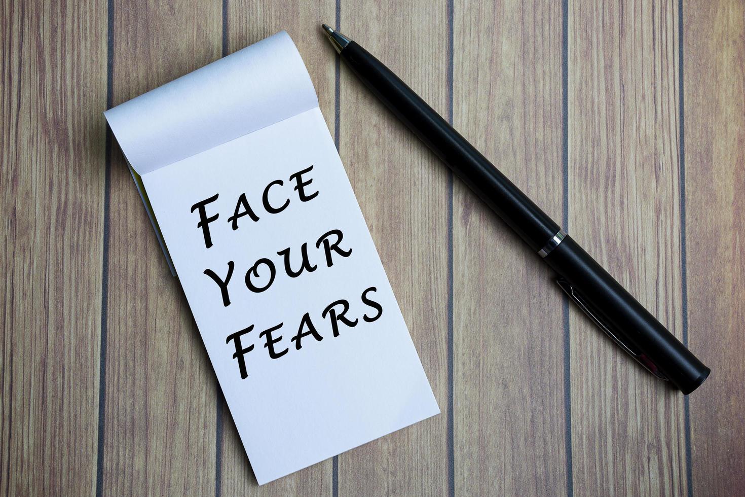 enfréntate al texto de tus miedos en el bloc de notas con un bolígrafo en un escritorio de madera. foto