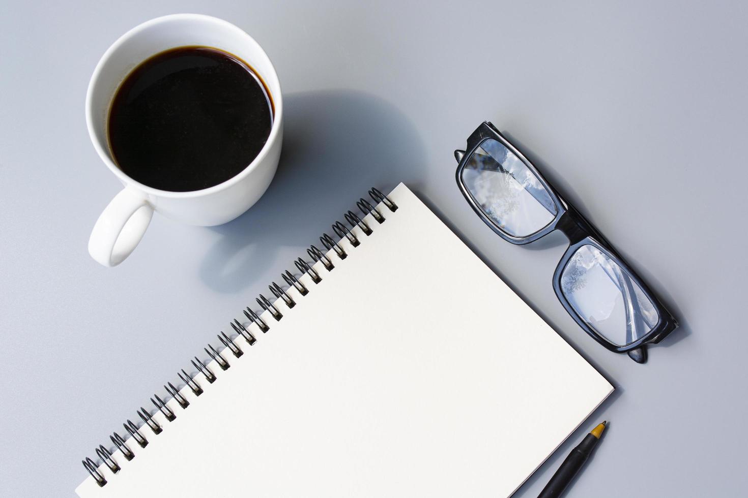 Notepad with cup of coffee and reading glasses on a desk. Directly above. photo